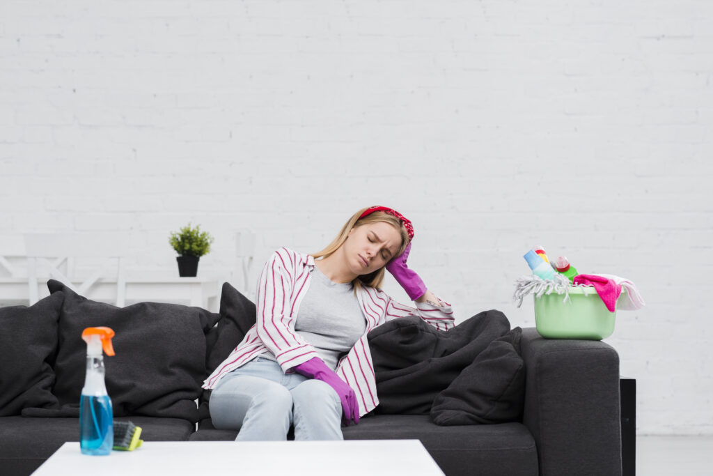 : Een flesje UF2000 geur- en vlekverwijderaar, met een sproeikop, staat op een houten tafel naast een stapel papieren handdoeken. Op de achtergrond is een vloerbedekking en een stoffen stoel te zien, die suggereren dat het product gebruikt kan worden voor het verwijderen van urinegeur en -vlekken uit vloerbedekking en stoffen meubels. Op het label van de fles is duidelijk de naam "UF2000" te zien.